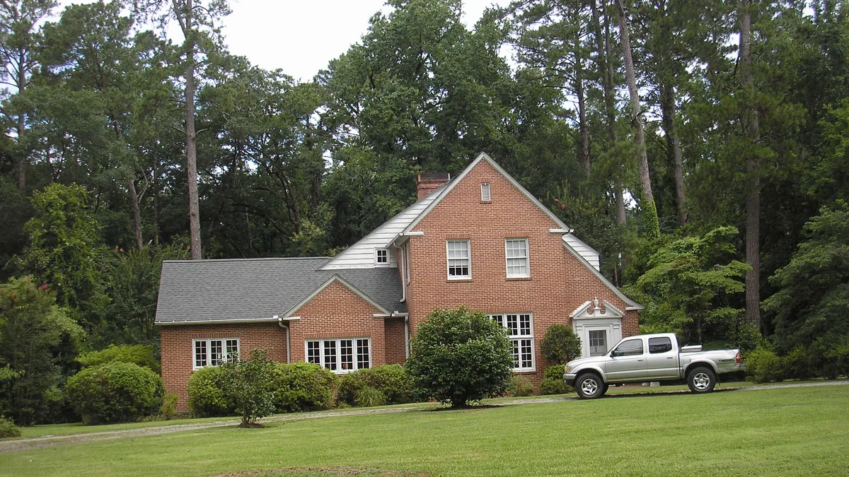 A red brick single-family house set among pine trees on a green lawn in Macon, Georgia