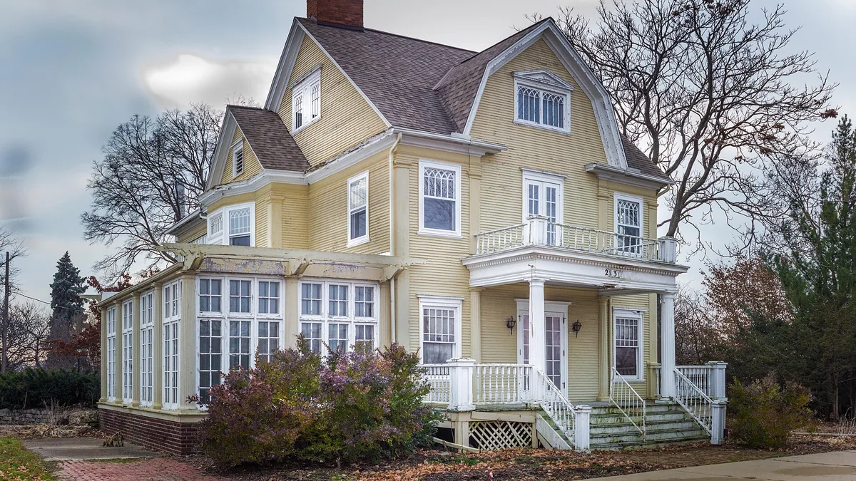 An older wood-frame house with weathered paint and a covered porch in Lansing, Michigan